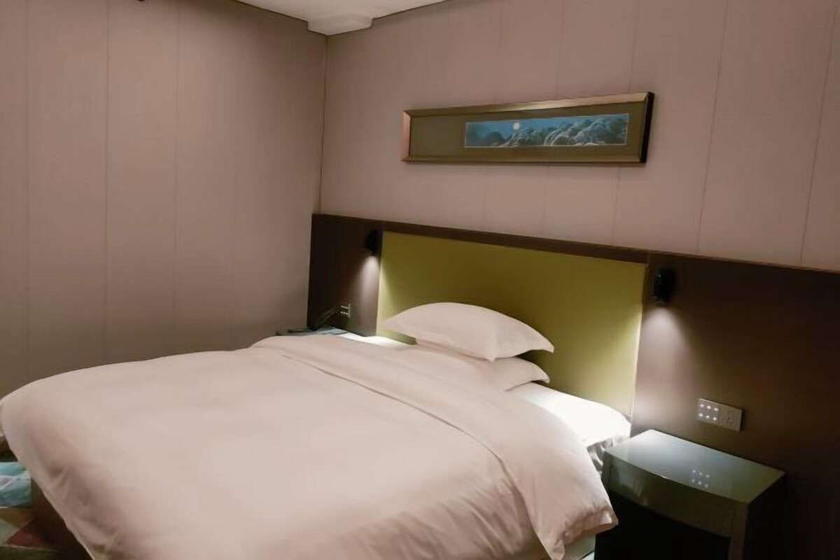 A neatly made bed with a headboard, a bedside table, and a wall-mounted light switch.