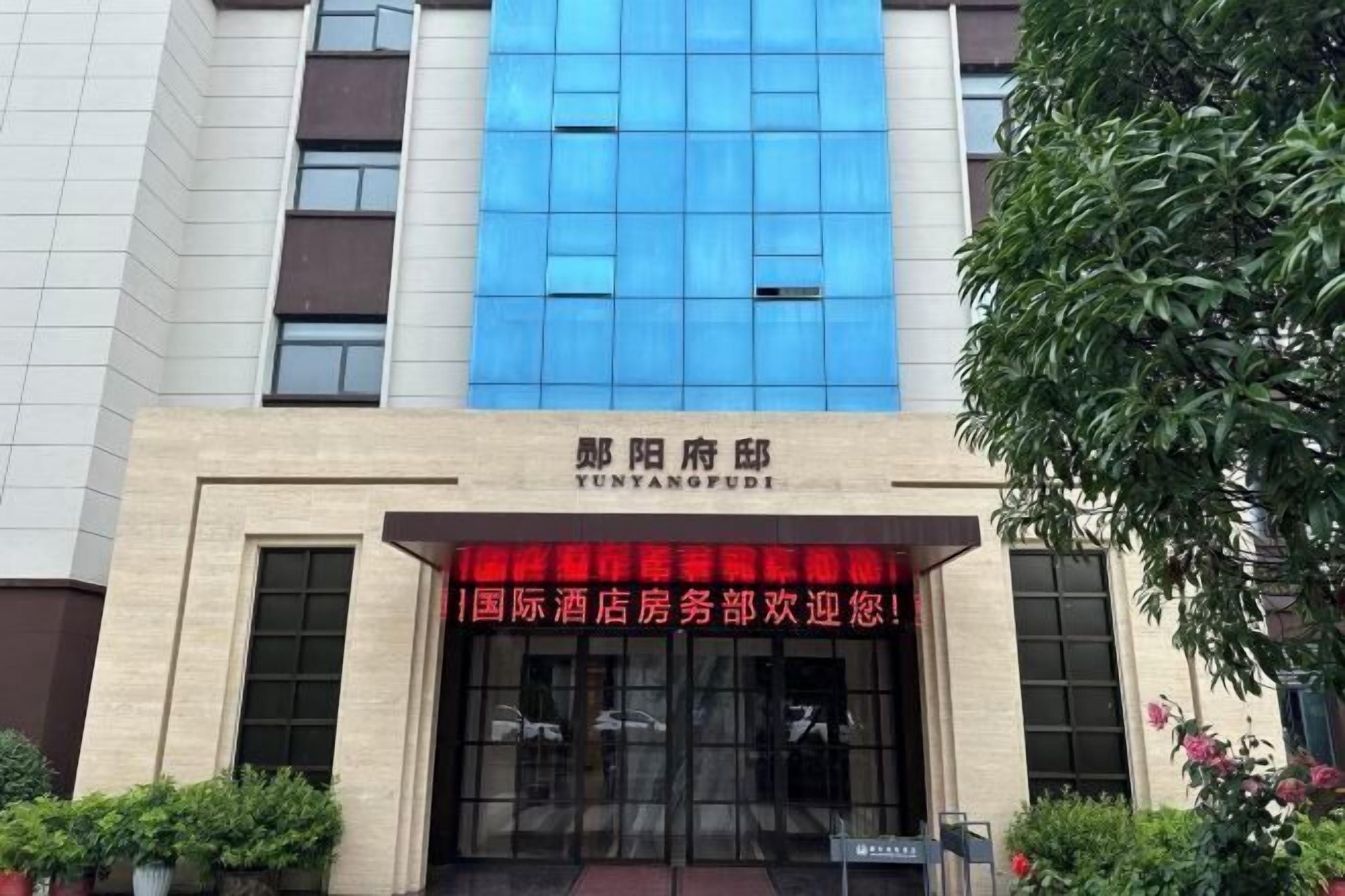 A hotel entrance with a blue glass facade and a red banner.