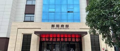 A hotel entrance with a blue glass facade and a red banner.