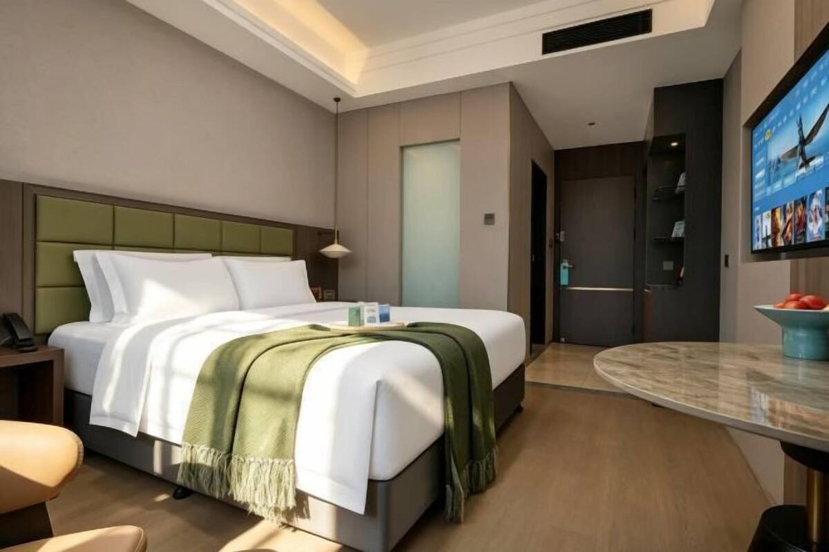 A modern hotel room with a bed, a desk, a chair, a TV, and a door.