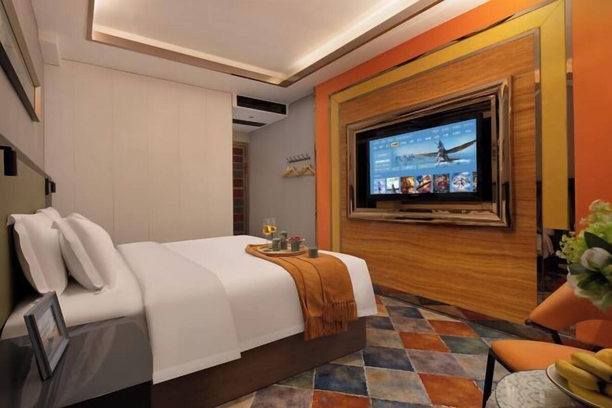 A modern hotel room with a large bed, a flat-screen TV mounted on the wall, and a colorful tiled floor.