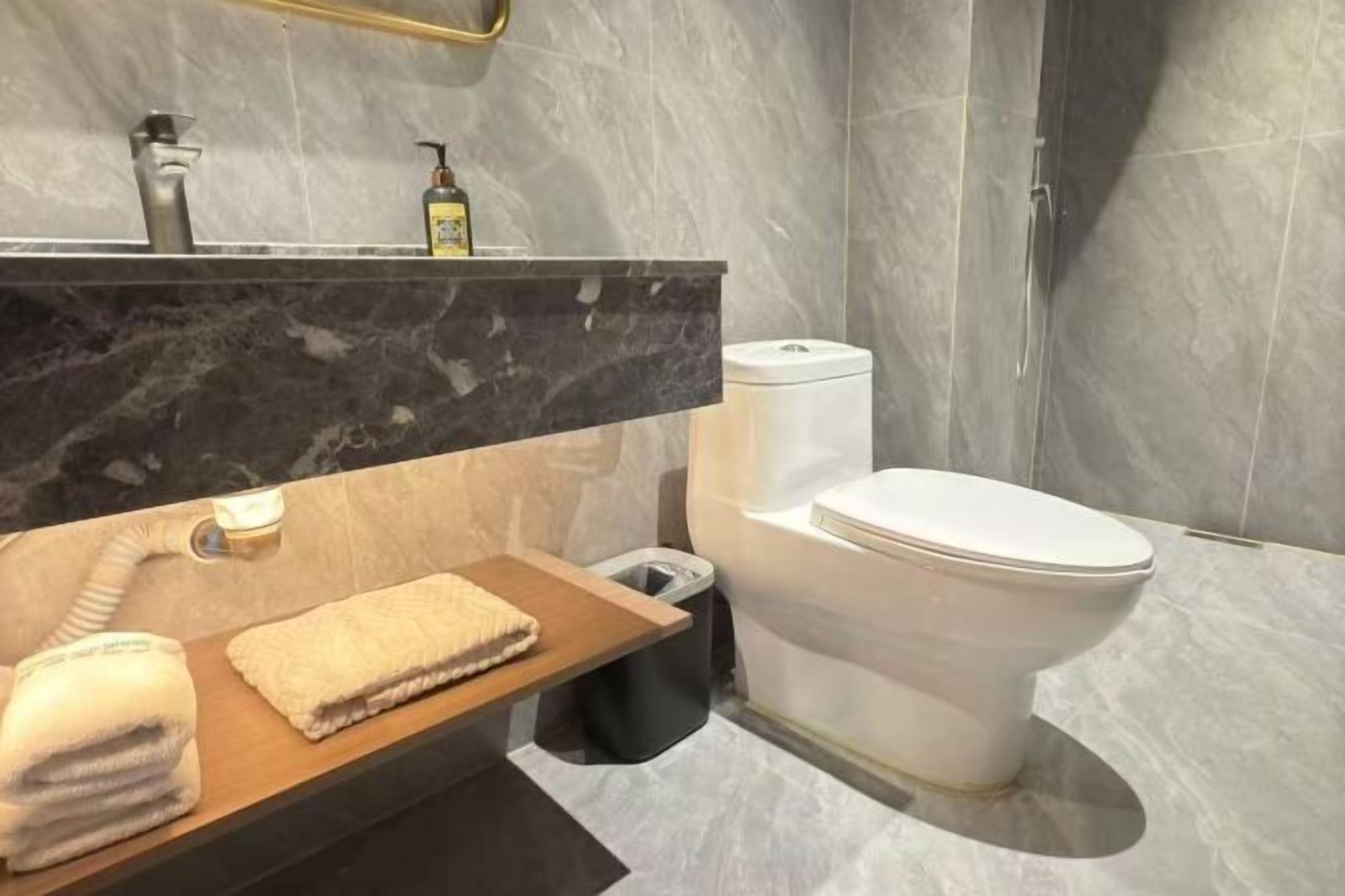 Un baño moderno con encimera de mármol, inodoro y cubo de basura.
