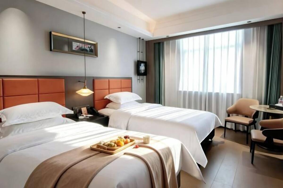 A hotel room with two beds, a dining area, and a TV on the wall.