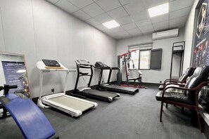 A fitness room with treadmills, a weight machine, and a blue exercise chair.