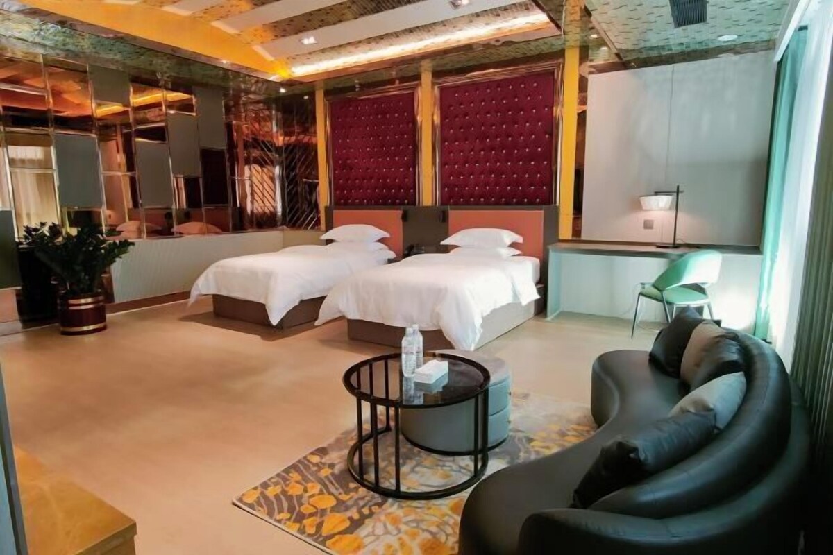 A hotel room with two beds, a sofa, a small round table, and a potted plant.