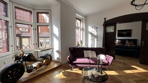 Un salón amplio con un ventanal grande, un sofá morado, una mesa de centro de cristal y una motocicleta.