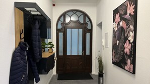 Un pasillo con puerta de madera, perchero, planta en maceta y un cuadro con motivos florales.
