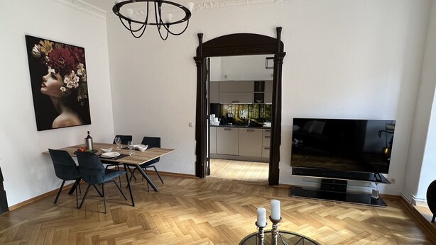 Una sala de estar moderna con comedor, televisor y cocina al fondo.