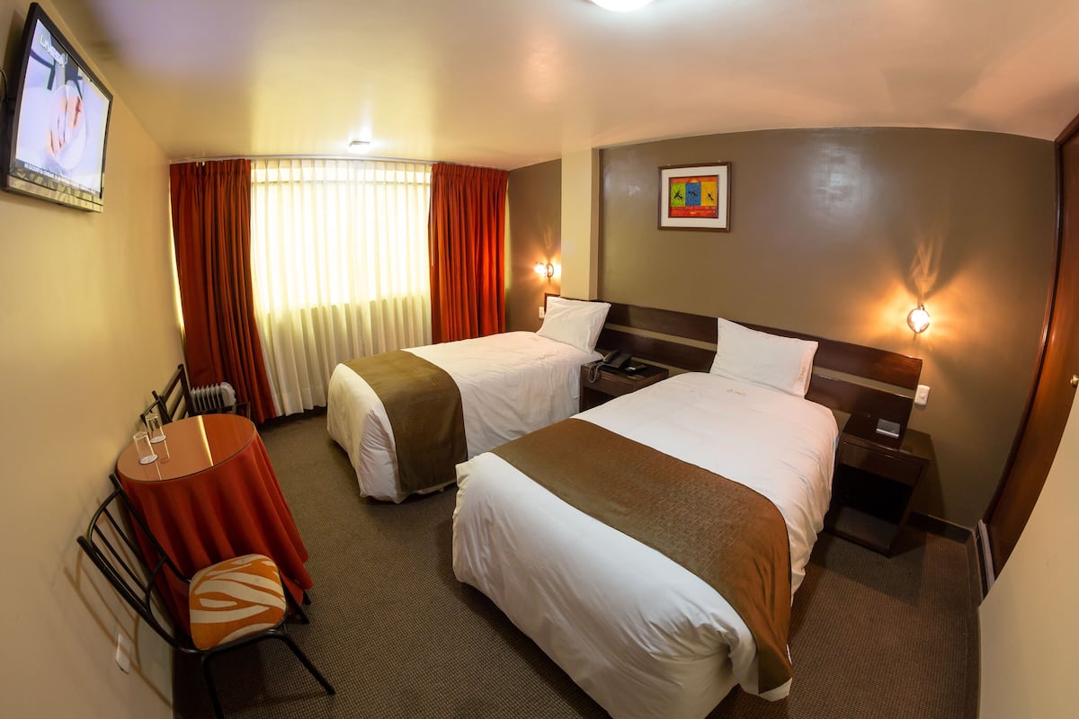 A hotel room with two beds, a desk with a chair, a TV, and a picture on the wall.