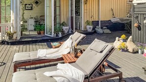 A wooden deck with two lounge chairs, a small table with a bottle and glasses, and potted plants. - Cozy home in Skutskär with sauna (Skutskär)