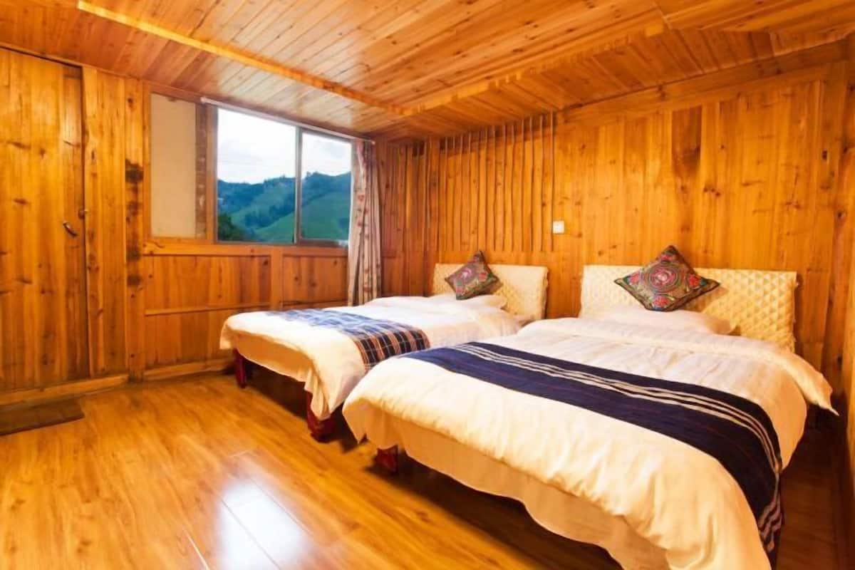 A wooden cabin room with two beds, a window, and a view of the outdoors.