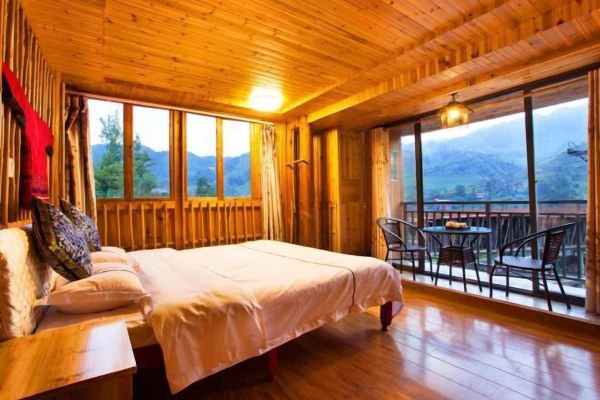 A wooden cabin room with a bed, a table, and chairs near large windows.