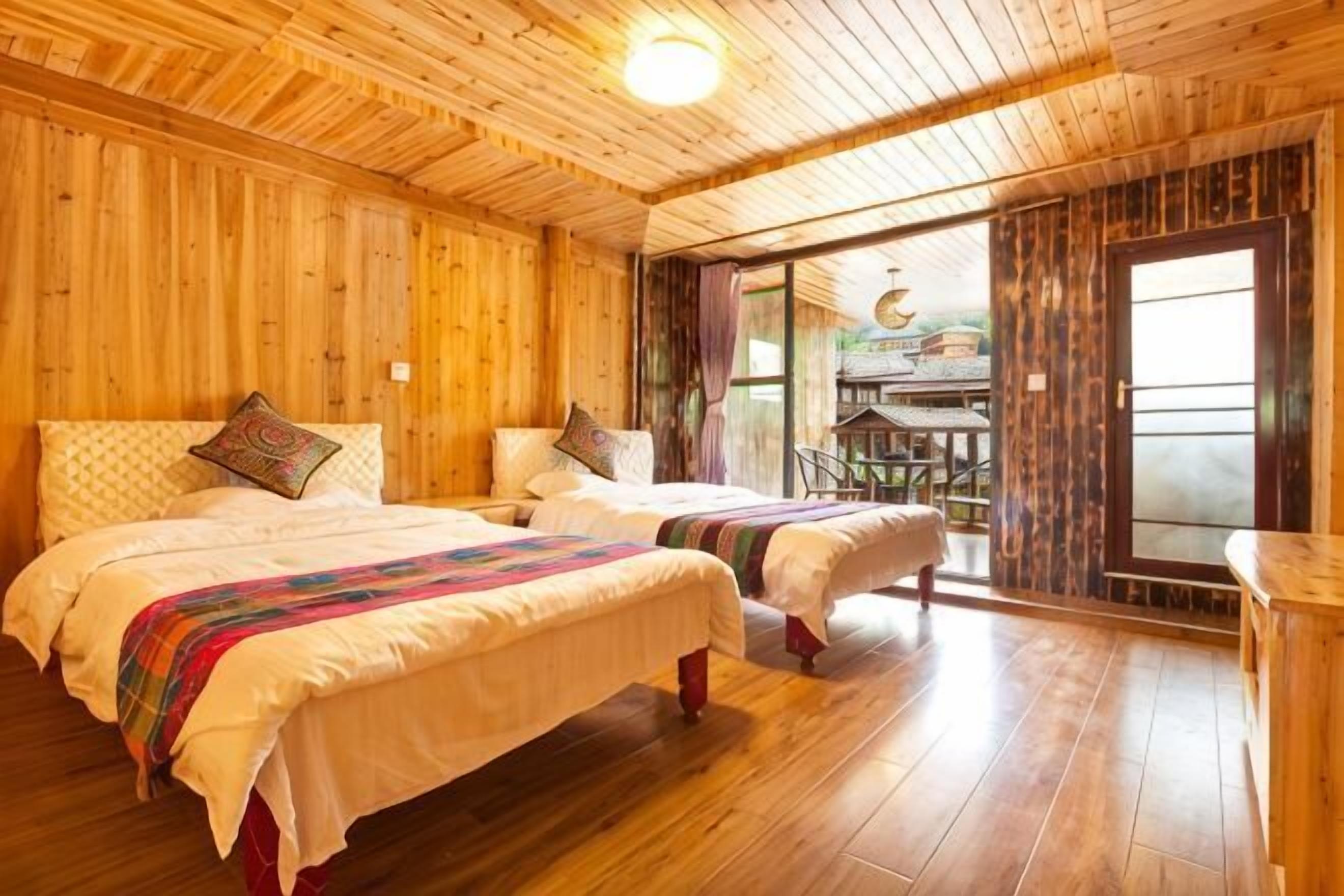 A wooden cabin-style room with two beds, a dining area, and a large window.