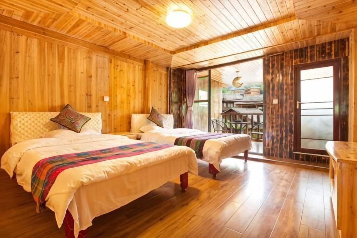 A wooden cabin-style room with two beds, a dining area, and a large window.