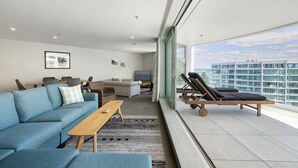 Ein modernes Wohnzimmer mit einem blauen Sofa, einem Holztisch und einem Balkon mit Liegestühlen.