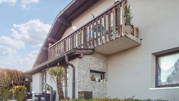 Ein modernes Gebäude mit einer Stein-Fassade, einem Balkon mit Holzgeländern und Pflanzkübeln.