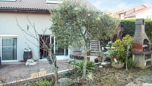 Ein Wohnhausgarten mit Terrasse, Steingrill und vielfältigen Pflanzen.