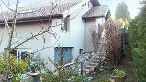 Ein modernes, zweigeschossiges Haus mit Ziegeldach, einer sichtbaren Treppe und einem Gartenbereich mit verschiedenen Pflanzen und einem großen Topfpflanzen.