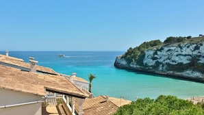 Blick auf die Küste mit einem Gebäude, das ein Ziegeldach und einen Balkon mit Blick auf türkisfarbenes Wasser und eine felsige Klippe hat.