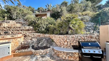 A stone barbecue area with a grill, a stone wall, and a wooden deck.