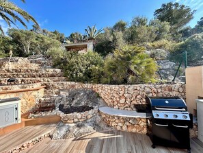 A stone barbecue area with a grill, a stone wall, and a wooden deck.