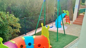 Ein Kinderspielbereich mit Rutsche, Schaukeln und einer bunten Spielanlage.