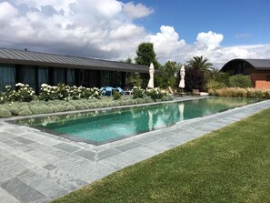 Une piscine bordée de pierres, entourée d’une pelouse bien entretenue et de diverses plantes.