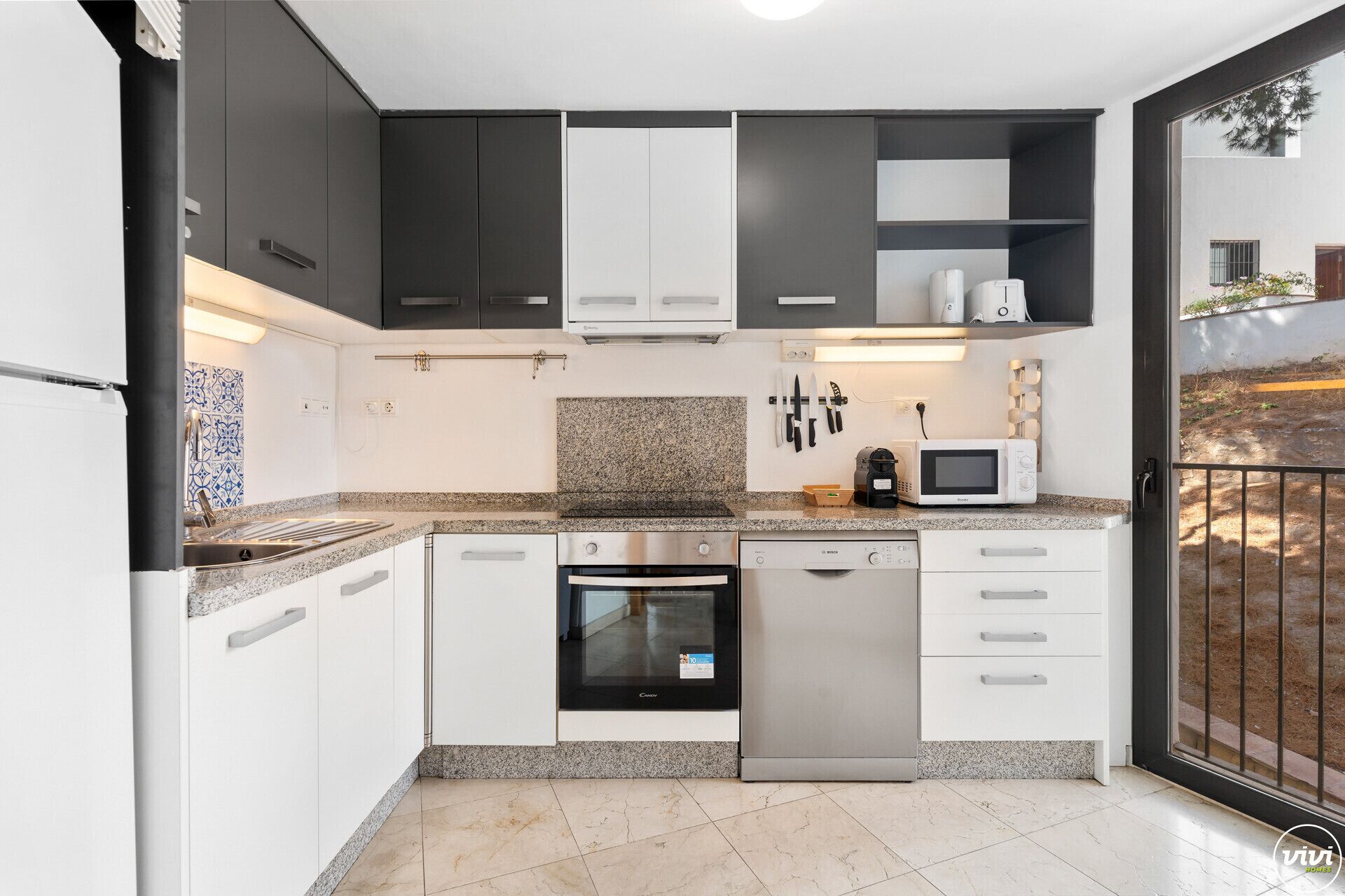 Een moderne keuken met witte en donkere kastjes, een granieten aanrecht, een vaatwasser, een oven en een magnetron.