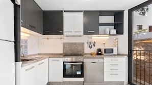 A modern kitchen with white and dark cabinets, a granite countertop, a dishwasher, an oven, and a microwave.