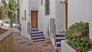 A building with a wooden door labeled "CASA ALA," a staircase with blue steps, and a potted plant with pink flowers.