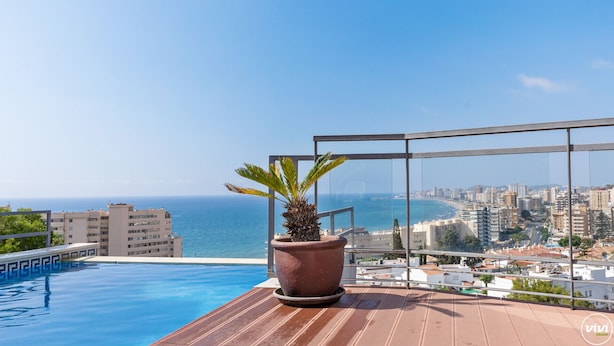 A rooftop pool with a view of the sea and cityscape.