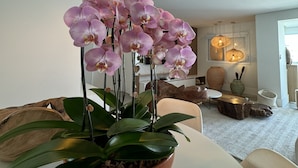 Una sala de estar con una orquídea en maceta, una mesa redonda y lámparas colgantes esféricas.