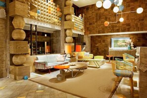 Relax in our stylish lobby with a sofa set, chairs, and coffee table, surrounded by unique geometric patterns and a staircase with a wooden railing.