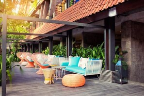 Relax in this inviting outdoor seating area with wicker chairs, a sofa, and ottomans, surrounded by lush greenery and a tiled roof.