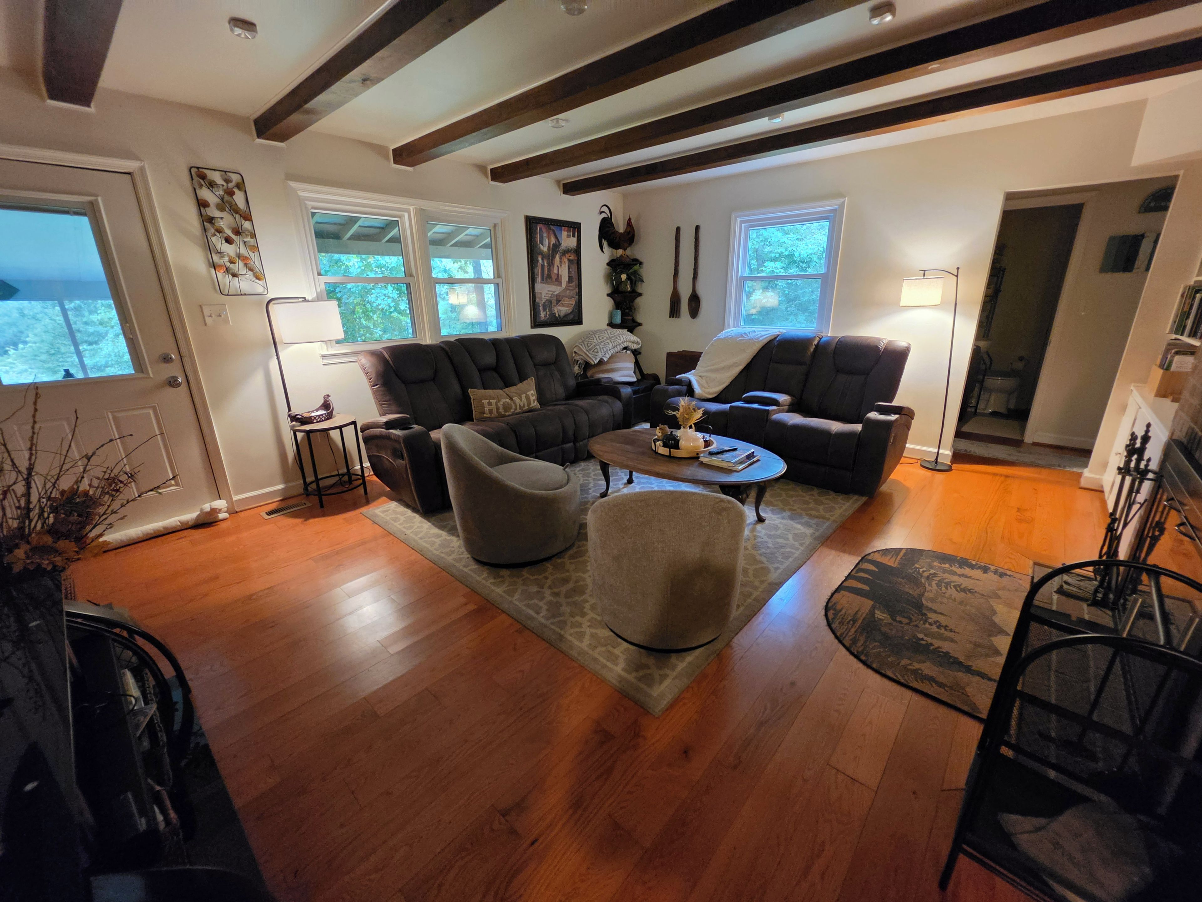 A living room with a sofa, armchairs, a coffee table, and a rug. There are windows, a door, and a lamp.