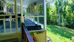 A covered porch with a view of a lush garden and trees.
