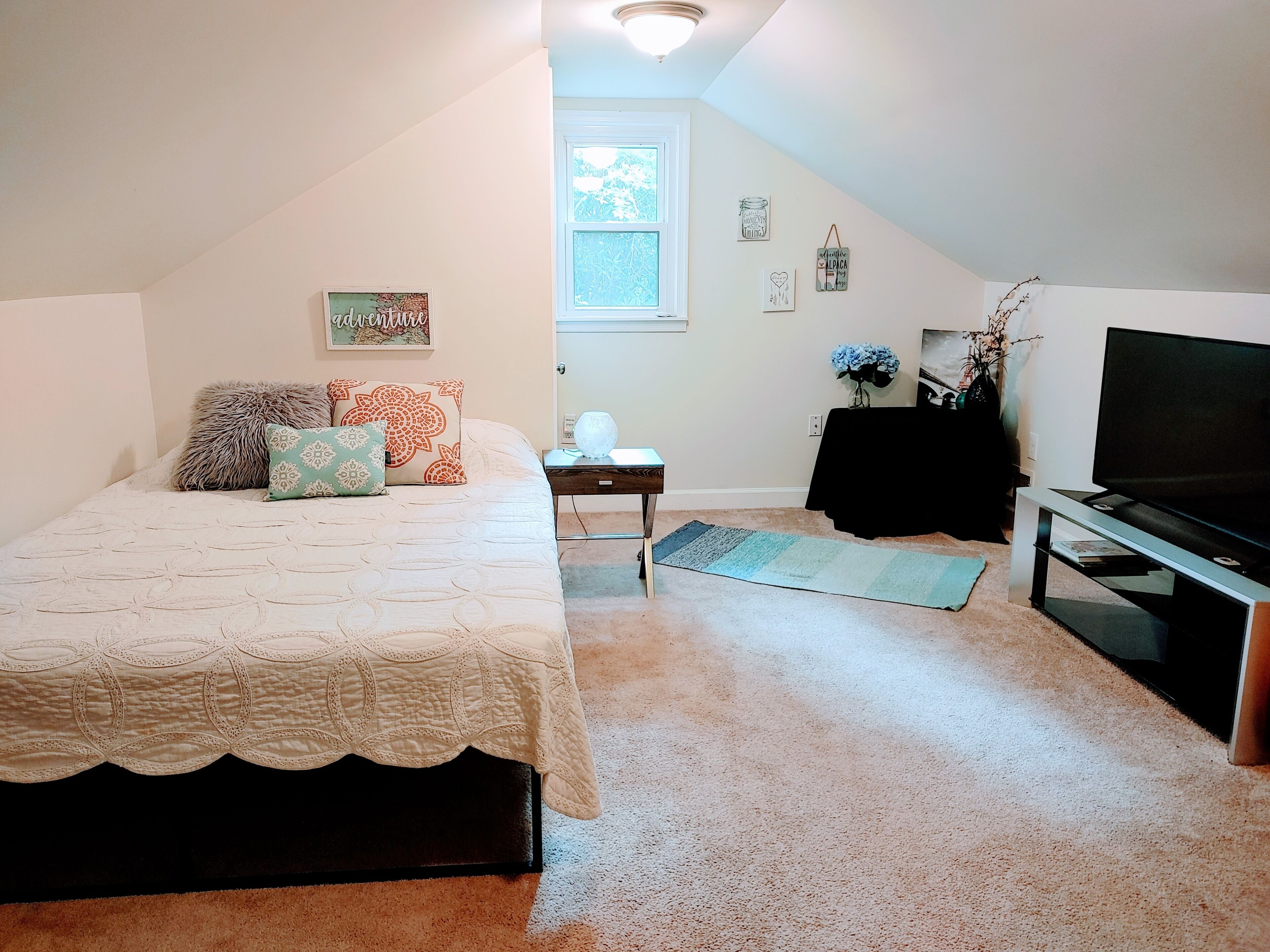A bedroom with a bed, a TV, a small table, and a window.