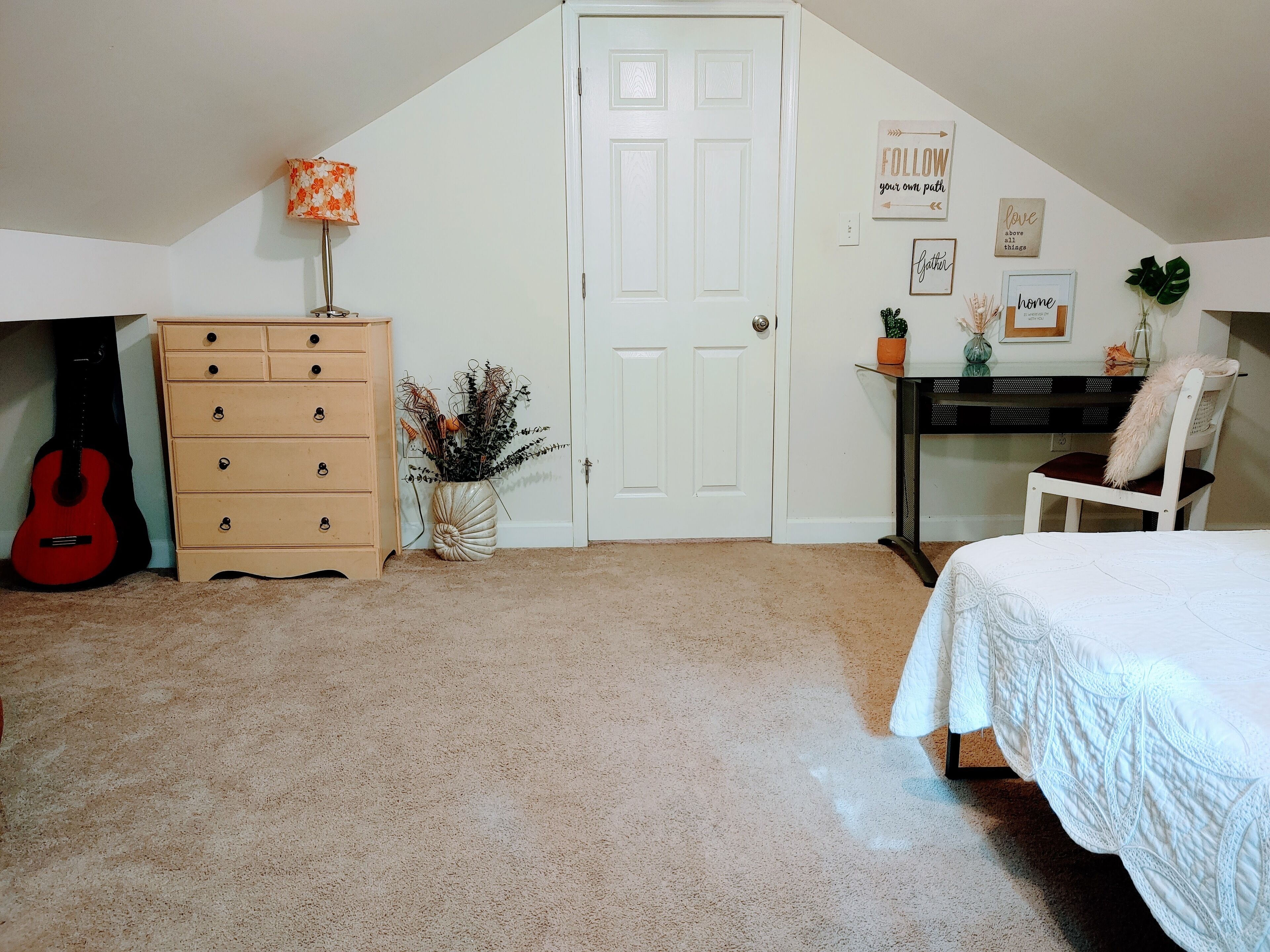A bedroom with a bed, dresser, guitar, door, and wall decorations.