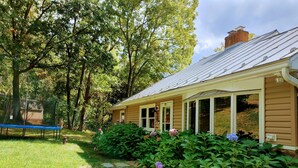 A house with a covered porch, surrounded by lush greenery and a trampoline.