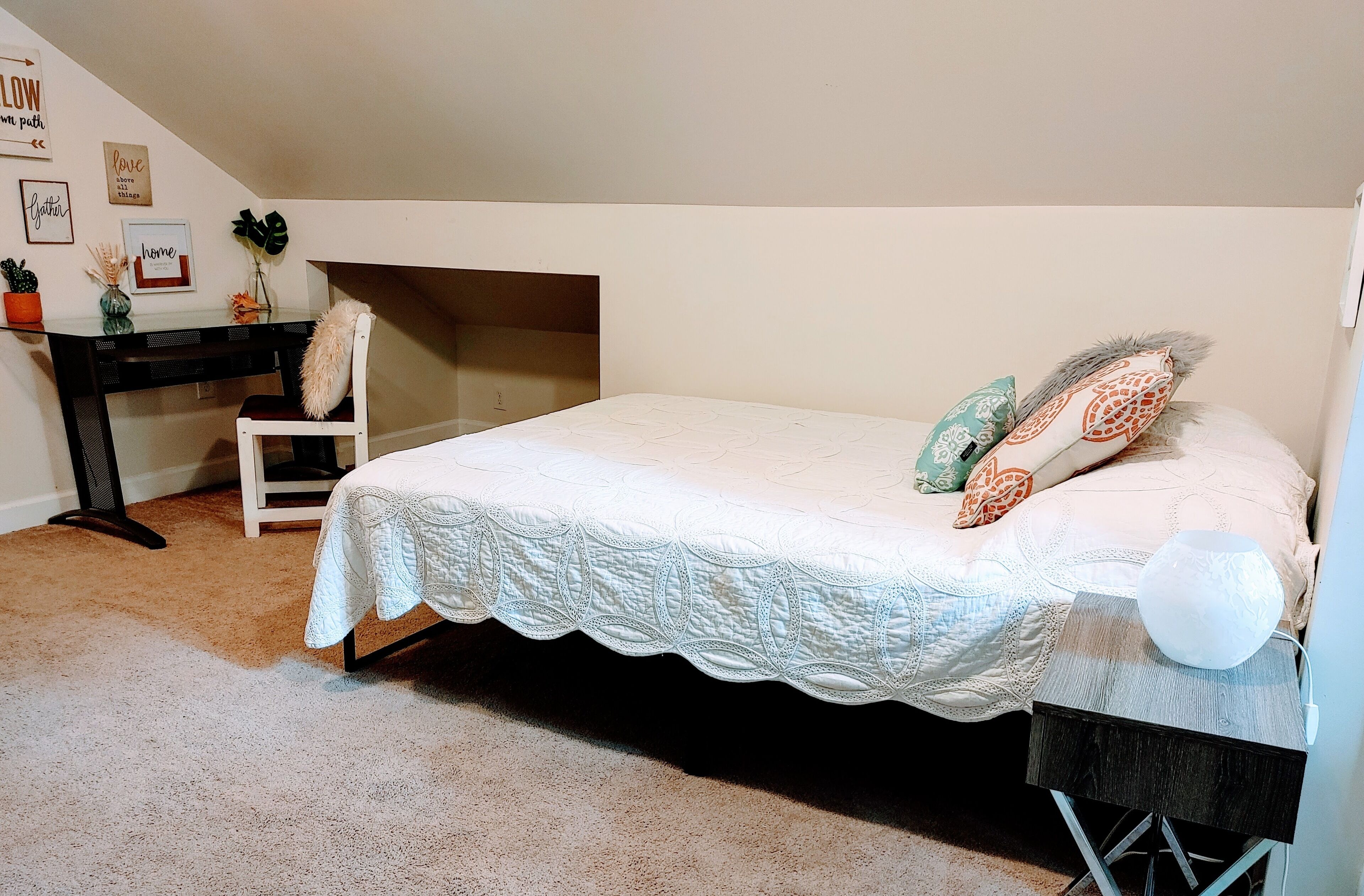 A bedroom with a bed, a desk, a chair, and a small table.