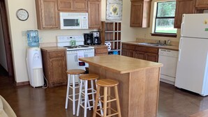 Una cocina con armarios de madera, una isla central con taburetes, un refrigerador y una cafetera.