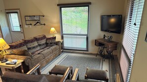 Un salon confortable avec un canapé, des fauteuils, une table basse, une lampe, une machine à coudre et un téléviseur.
