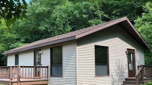 Une cabane de plain-pied dotée d’un porche à l’avant et d’une petite terrasse, entourée d’une végétation luxuriante.