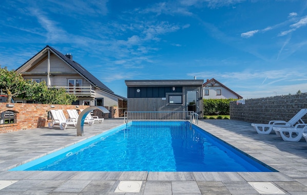 Une piscine avec des chaises longues, un mur en briques et un bâtiment moderne doté d’un balcon.