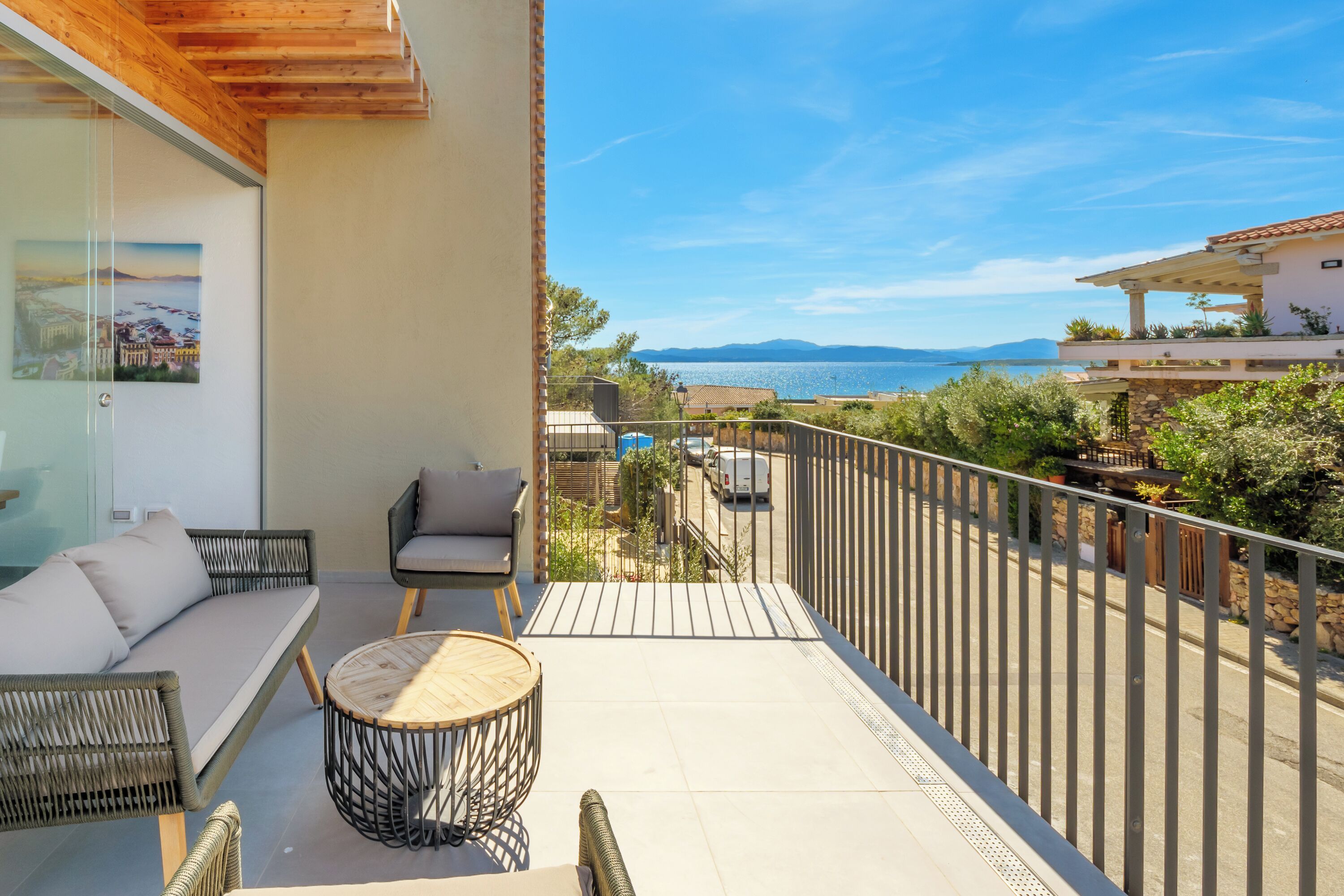 A balcony with wicker furniture, a round table, and a view of the sea and mountains.