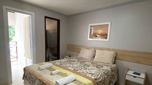 A bedroom with a bed, a nightstand, a door, and a painting on the wall. - Pousada Pérola do Mar (Tamandaré)