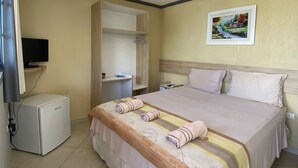 A hotel room with a bed, a small refrigerator, a TV, a painting on the wall, and a bathroom visible through an open door. - Pousada Pérola do Mar (Tamandaré)