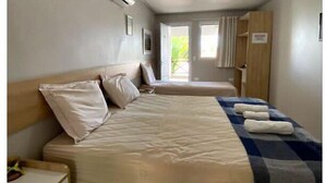 A single bed with a checkered blanket, a bedside table, a wardrobe, and a window with curtains. - Pousada Pérola do Mar (Tamandaré)