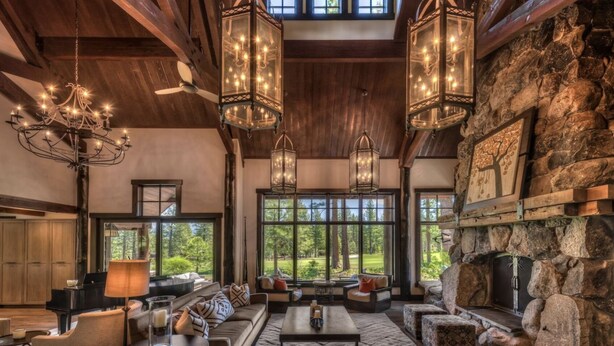 Un salón amplio con chimenea de piedra, ventanas grandes que ofrecen vistas al exterior y múltiples lámparas colgantes.