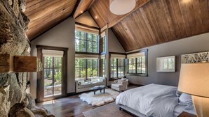 Un dormitorio con una cama grande, un sofá, una silla y una mesa. Hay ventanas amplias y vistas al exterior.